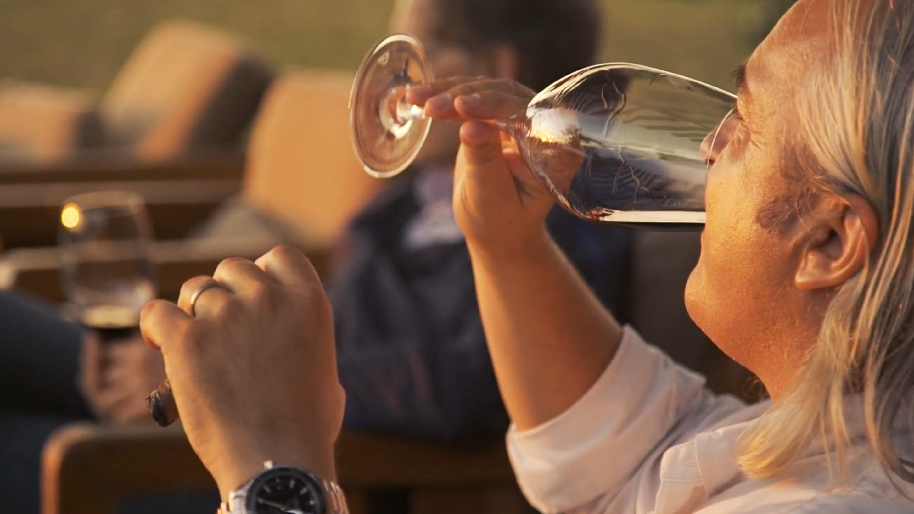 Two people toasting with wine glasses against a blurred outdoor background.